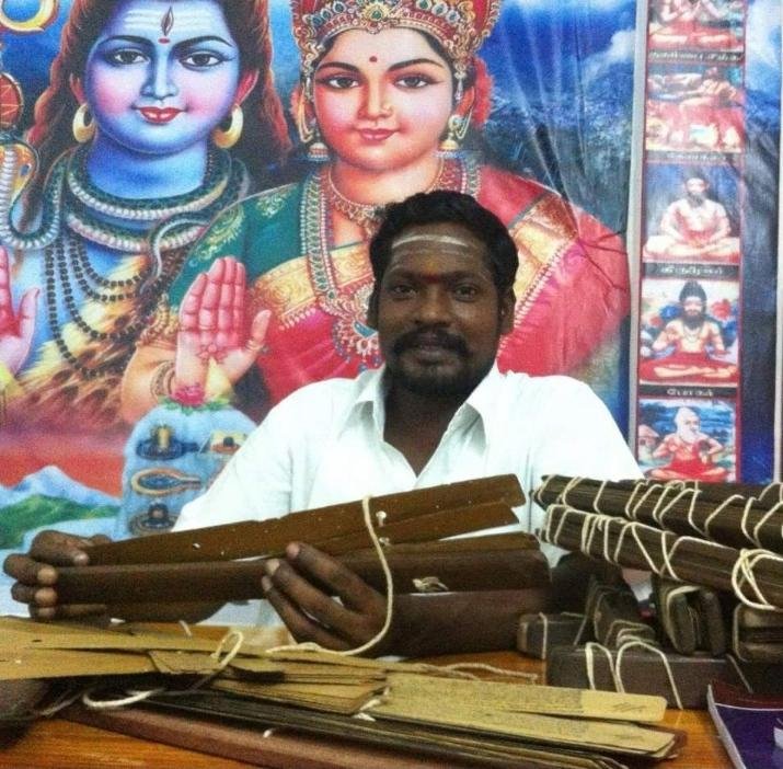 Guruji B.S. Vignesh Swamy holding palm-leaf manuscripts before a portrait of Lord Shiva and Goddess Parvati